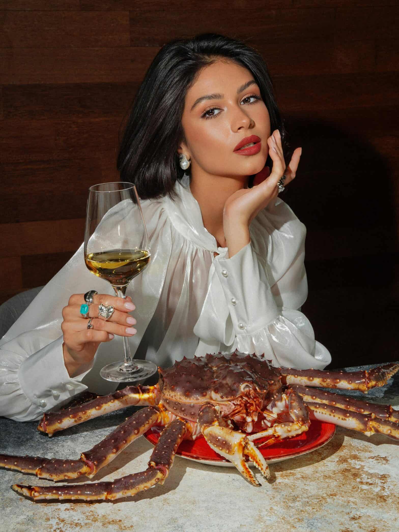 high class lady holding a glass of wine with a large crab on her plate